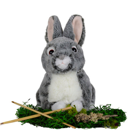 small round bunny plush toy, placed on green moss with some sticks in front of it.