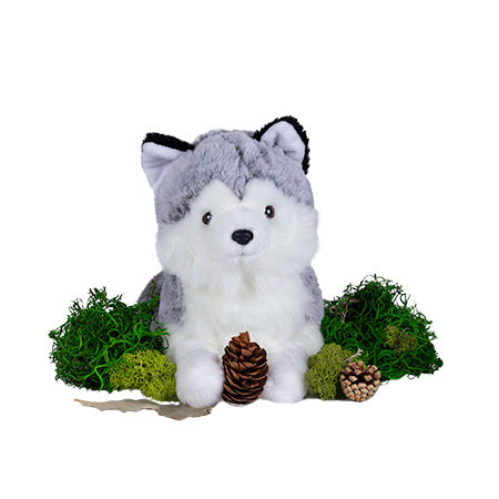 silver fox stuffed animal resting on green moss with a small pine cone between it's paws.